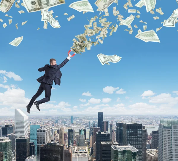 Полет уверенный красивый бизнесмен с магнитом привлекает купюры долларов. город Нью-Йорк на фоне — стоковое фото