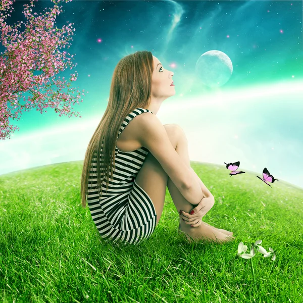 Женщина, сидящая на на зеленом лугу, преграждает планету, смотрящую на звездное небо — стоковое фото