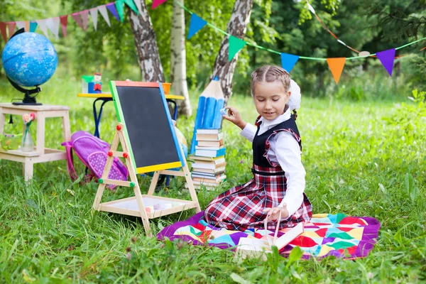 Счастливая детская девочка ребенка школьницы, сидящая на траве, читая книгу — стоковое фото