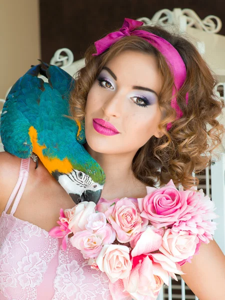 Portrait of young beautiful woman in colorful dress with flowers it in doll style with ara on her shoulder — стоковое фото