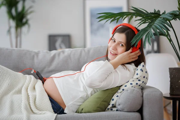 Изображение беременная женщина, лежа на диване, послушать музыку в наушниках — стоковое фото