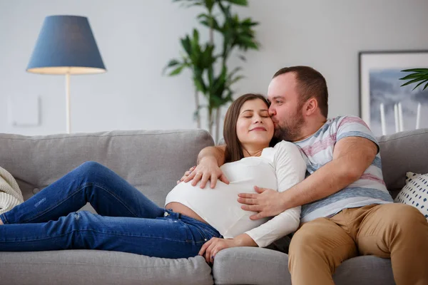 Фото обнимать беременная женщина и мужчина на сером диване — стоковое фото