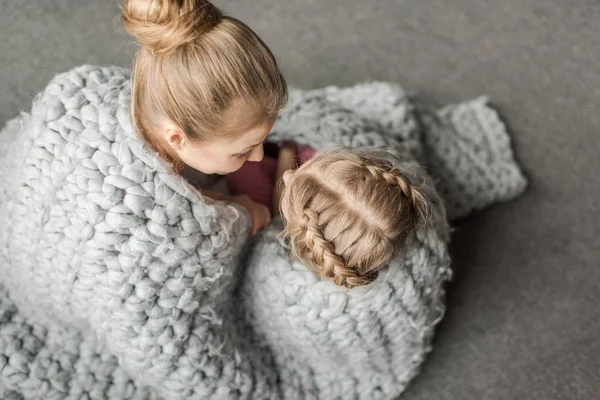 Вид сверху матери и дочери обнимает и сидит на полу с шерстяным трикотажным одеялом — стоковое фото