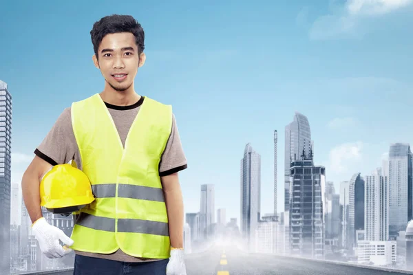Привлекательные Азии Строительный Рабочий Холдинг Желтый Шлем Фоне Городского Пейзажа — стоковое фото