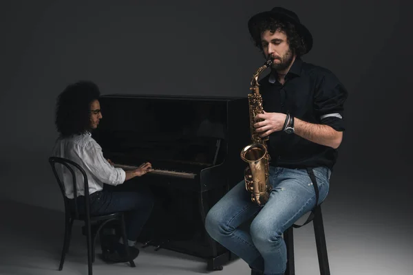 Человек играет саксофон, в то время как его партнер, играть на фортепиано размыта на фоне — стоковое фото