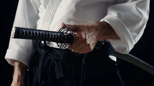 Мастер айкидо, традиционные Самурай Хакама одежде держит его японский меч в ножны. Он находится в Spotlight тьма окружает его. Выстрел, изолированные на черном фоне — стоковое фото