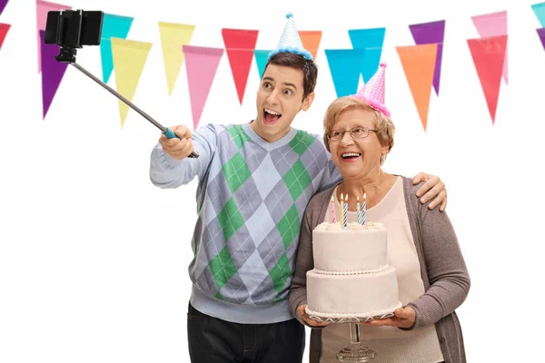Человек и пожилая женщина с торт ко дню рождения, принимая selfie — стоковое фото
