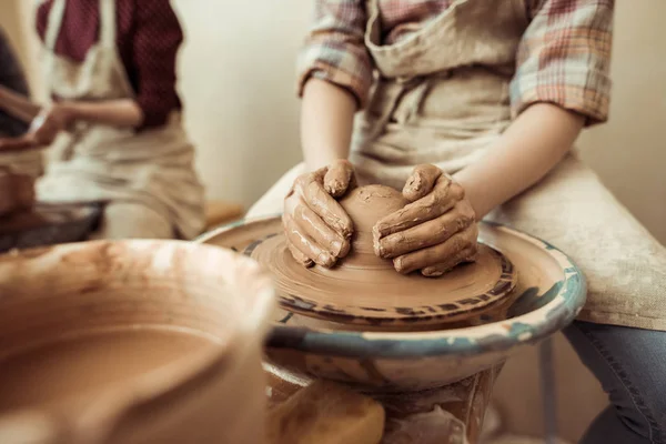 Закройте руки ребенка, работающие на гончарном колесе в мастерской — стоковое фото