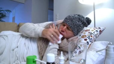 Человек, одетый В теплую шапку и шарф в постели кашляет и использует спрей для горла — стоковое видео