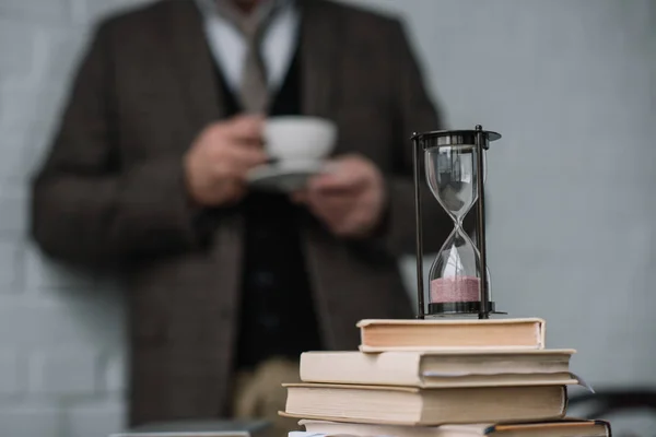 Крупным Планом Стека Книг Песочные Часы Человеком Пить Кофе Размыта — стоковое фото