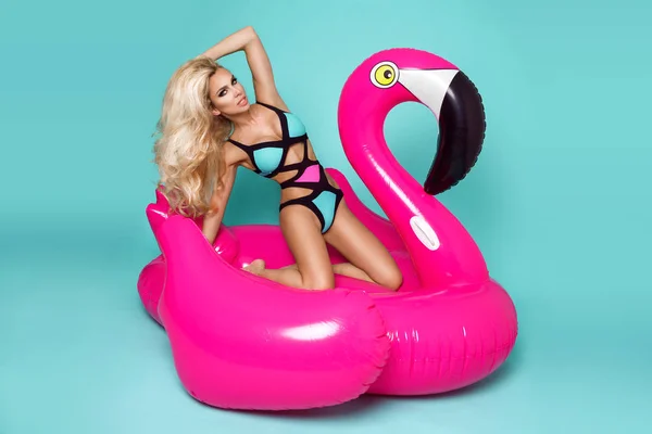 Потрясающие сексапильная блондинка модель в красочных бикини, лежит на розовый фламинго — стоковое фото