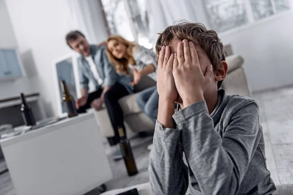 Исчерпаны мальчик, скрывая его лицо, а его родители, обсуждая их развода — стоковое фото