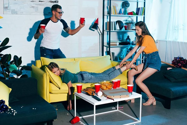 Smiling Man Holding Plastic Cups Looking Girl Pulling Drunk Female — стоковое фото