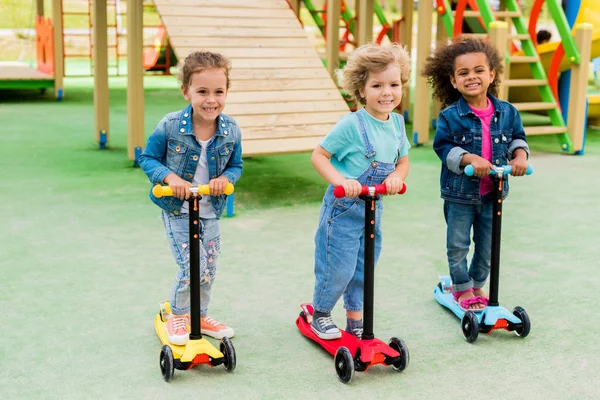 Three Multicultural Adorable Little Children Riding Kick Scooters Playground — стоковое фото