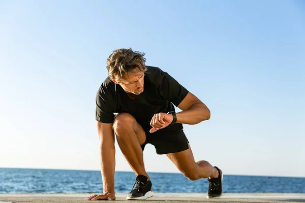 Handsome Adult Sprint Runner Looking Fitness Tracker While Standing Start — стоковое фото