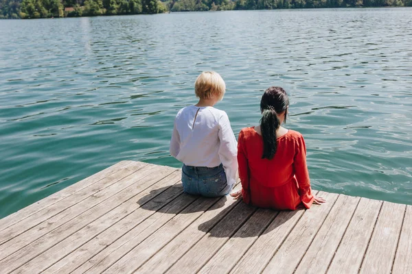 Вернуться Мнение Двух Молодых Стильных Женщин Сидя Деревянный Причал Озере — стоковое фото