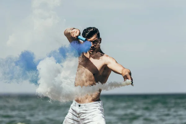 Attractive Shirtless Man Dancing Blue White Smoke Sticks Front Ocean — стоковое фото