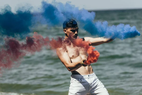 Shirtless Man Dancing Red Blue Smoke Sticks Front Ocean View — стоковое фото