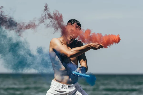 Attractive Shirtless Man Dancing Red Blue Smoke Sticks Front Ocean — стоковое фото