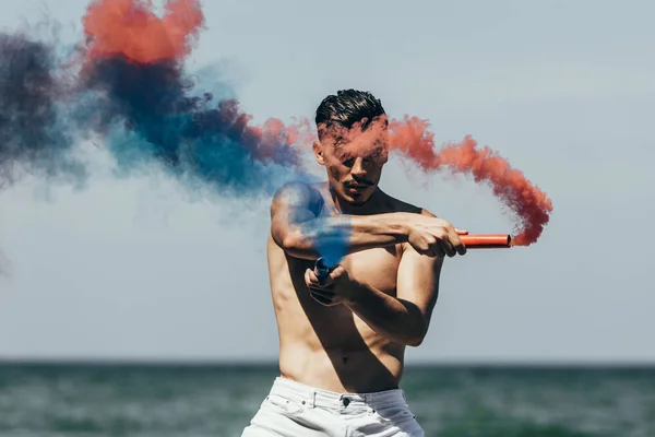 Handsome Shirtless Man Red Blue Smoke Sticks Front Ocean View — стоковое фото