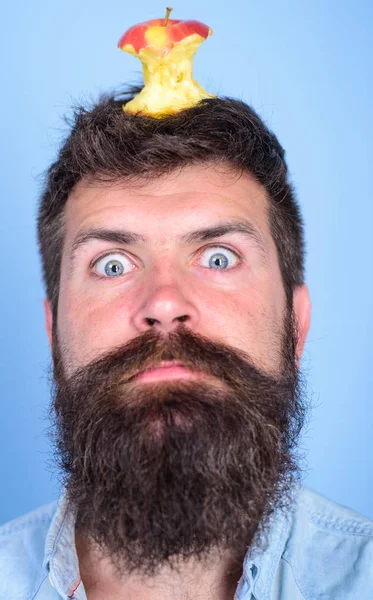 Hipster shocked face with apple stump target on head blue background, close up. Weight loss goal. Man handsome hipster long beard almost eaten apple stump on head as target. Live target concept — стоковое фото
