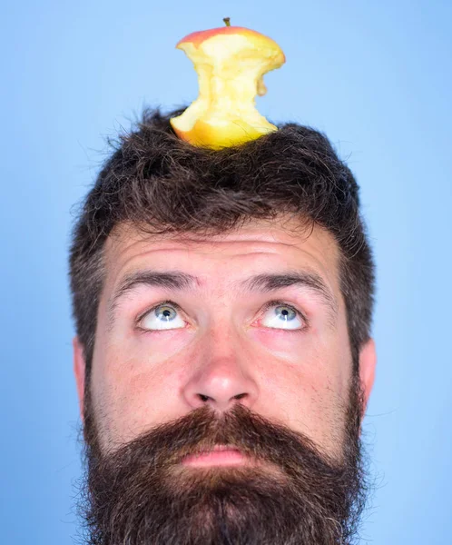 Man handsome hipster long beard almost eaten apple stump on head as target. Live target concept. Weight loss goal. Hipster surprised face with apple stump target on head blue background, close up — стоковое фото