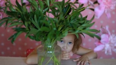 Child girl hides in a with peonies. Baby playing with pink peony flowers. — стоковое видео