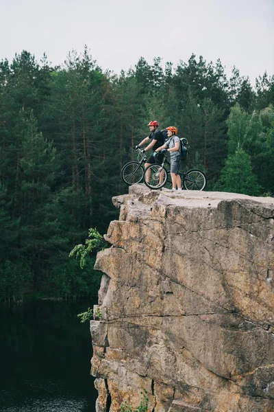 Side View Young Trial Bikers Standing Rocky Cliff Blurred Pine Стоковое Фото