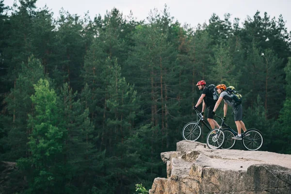 Side View Young Trial Bikers Standing Rocky Cliff Blurred Pine Стоковая Картинка