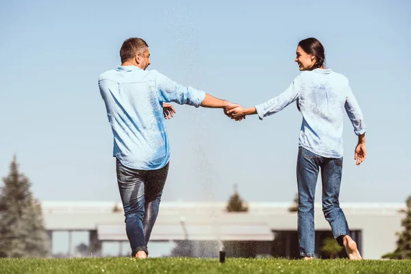 Rear View Couple Holding Hands Dancing Automatic Watering Green Lawn — стоковое фото