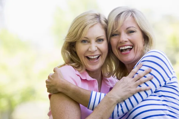 Две женщины, на открытом воздухе обнимающие и улыбающиеся — стоковое фото