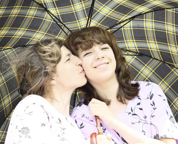 Мать целует дочь под клетчатый зонтик Лицензионные Стоковые Фото