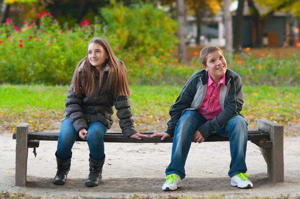 Застенчивая(ый) мальчик и девочка, сидя в парке и слегка касаясь друг друга fi — стоковое фото