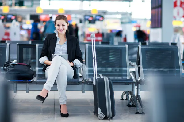 Молодая женщина пассажир в аэропорту, с помощью своего планшетного компьютера Лицензионные Стоковые Изображения